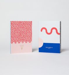 two notebooks sitting next to each other on a white surface with red and blue designs