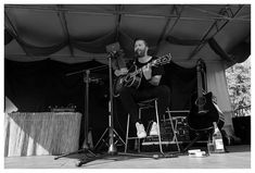 a man sitting on top of a chair while playing an acoustic guitar in front of a microphone