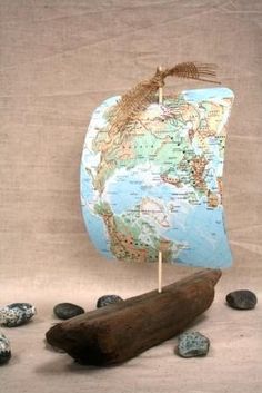 a small wooden boat with a map on it and rocks around it, sitting on a cloth covered surface