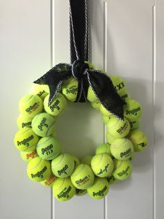 a wreath made out of tennis balls hangs on the wall with a black ribbon around it