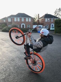 a young boy is doing tricks on an orange bike in the middle of the street