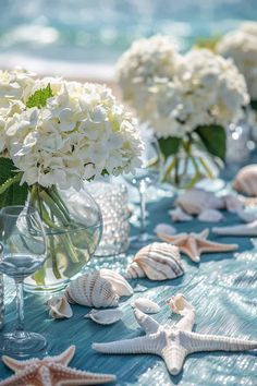 white flowers and seashells are arranged in vases on a blue table cloth