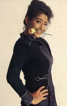 a woman with her hands on her hips wearing a black jacket and holding a banana in her mouth