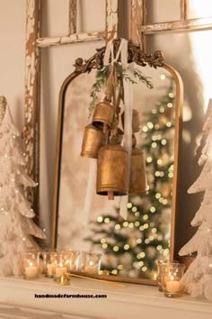 a mantle with candles and christmas trees in front of a mirror that has bells hanging from it