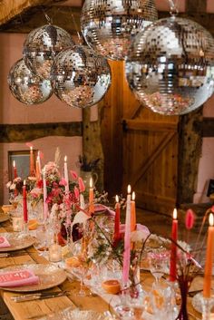 a long table is set with candles, plates and napkins as well as disco balls hanging from the ceiling