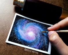 a person is holding a pencil and drawing the galaxy