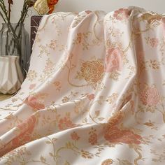 a vase with some flowers in it next to a blanket on a bed that is covered by a pink and gold floral print