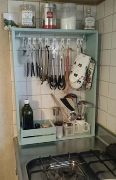 a stove top oven sitting under a shelf filled with utensils and other kitchen items