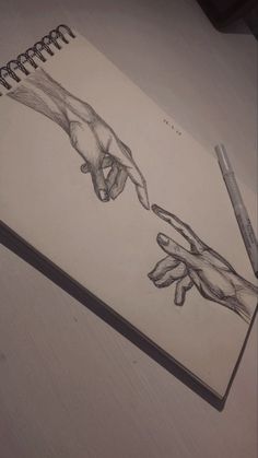 a pencil drawing of two hands reaching for each other's hand, on top of a notebook