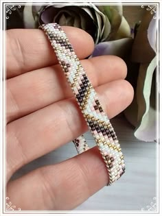 a hand holding a beaded bracelet in front of a flower arrangement with white and brown beads