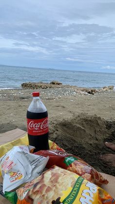 a bottle of coca cola sitting on top of a sandy beach next to the ocean