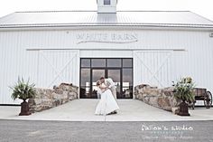 a bride and groom kissing in front of a white barn