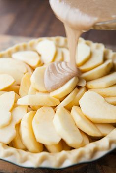 someone is pouring peanut butter on top of apple slices in a pie pan with the crust ready to be baked