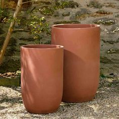 two large clay pots sitting next to each other on top of a gravel ground in front of a stone wall