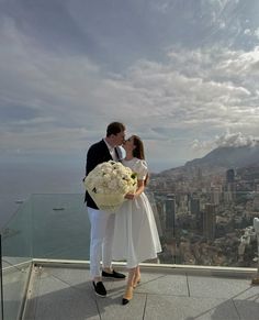 a man and woman standing on top of a building next to each other holding flowers