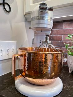 a kitchen mixer sitting on top of a counter next to a potted green plant