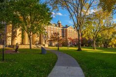 a walkway in the middle of a grassy area with trees on both sides and an old building in the background