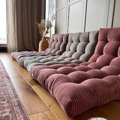 a pink couch sitting on top of a wooden floor next to a window with curtains