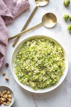 a bowl filled with shaved brussels sprouts next to two spoons and some nuts