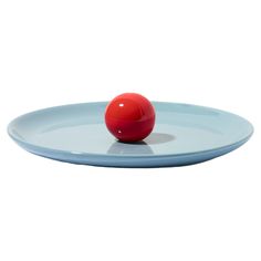 a red ball sitting on top of a blue plate in the middle of a white background