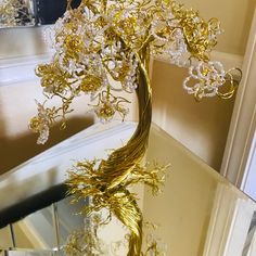 a gold tree sculpture sitting on top of a glass table next to a mirror in a room