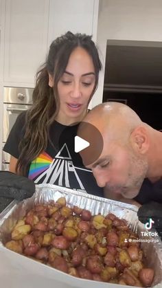 a man and woman looking at food in a pan