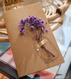 a brown card with purple flowers on it sitting on a table next to a cup