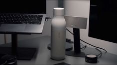 a white bottle sitting next to a laptop computer on a desk in front of a monitor