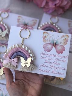 a hand holding a card with two butterfly keychains attached to it, and some flowers in the background