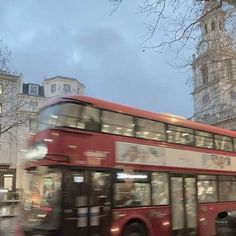 a red double decker bus driving past tall buildings