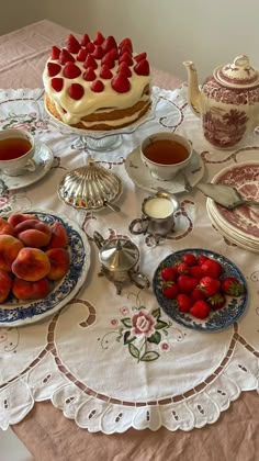 a table topped with plates of fruit next to a cake and tea set on top of a table