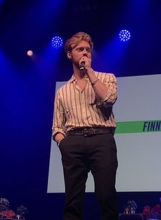 a man standing on top of a stage while holding a microphone in his hand and wearing a striped shirt