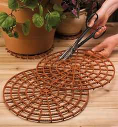 a pair of scissors cutting through an outdoor planter mat with plants in the background