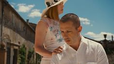 a man standing next to a woman in a white dress and hat on the street