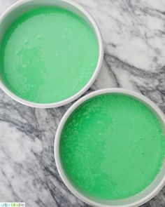 two white bowls filled with green liquid sitting on top of a marble countertop next to each other