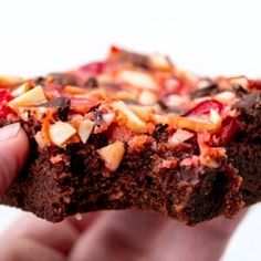 a hand holding up a piece of chocolate cake with nuts on it's side