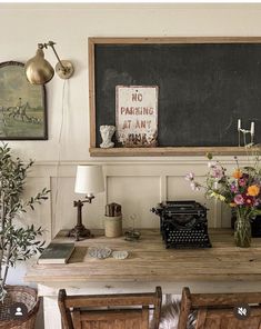 a table with two chairs and a blackboard on the wall above it, next to some flowers