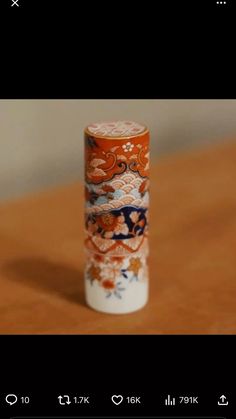 an orange and white vase sitting on top of a wooden table next to a cell phone