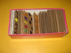 a pink box filled with lots of different types of cookies on top of a yellow table