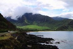 a car driving on the side of a road next to a body of water with mountains in the background