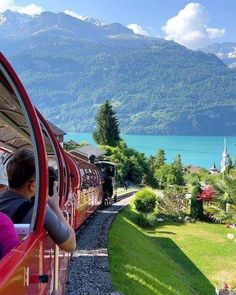 the train is going down the tracks by the water and mountains in the distance with people on it