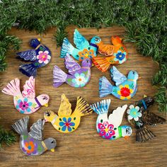 several colorful birds are sitting on a table next to some plants and branches, one is painted with bright colors