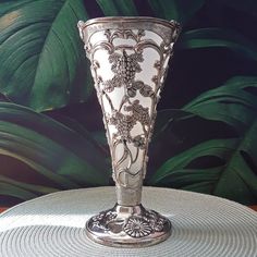 a silver vase sitting on top of a table next to a plant wallpapered background