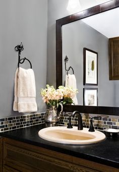 a bathroom sink sitting under a mirror next to a vase with flowers on top of it