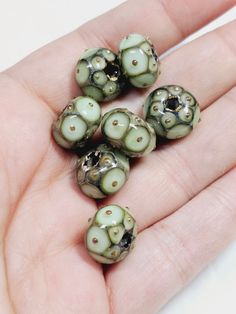 five green and black beads sitting on top of a hand