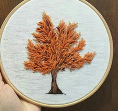 someone is holding up a cross stitched picture of a tree with orange leaves on it