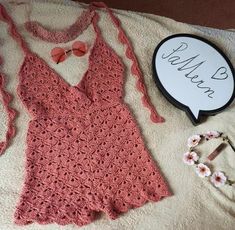 a pink crocheted dress and accessories laid out on a white towel next to a sign