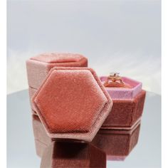 two wedding rings sitting on top of pink velvet jewelry boxes, one in the shape of a hexagon