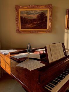 an old piano with music sheets on it in front of a painting and framed artwork