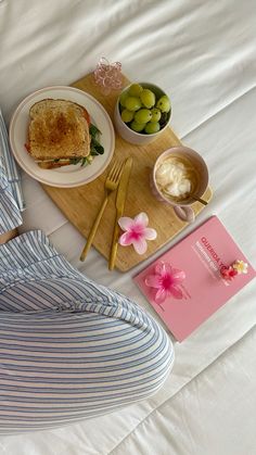 a person sitting on a bed with some food and a book in front of them